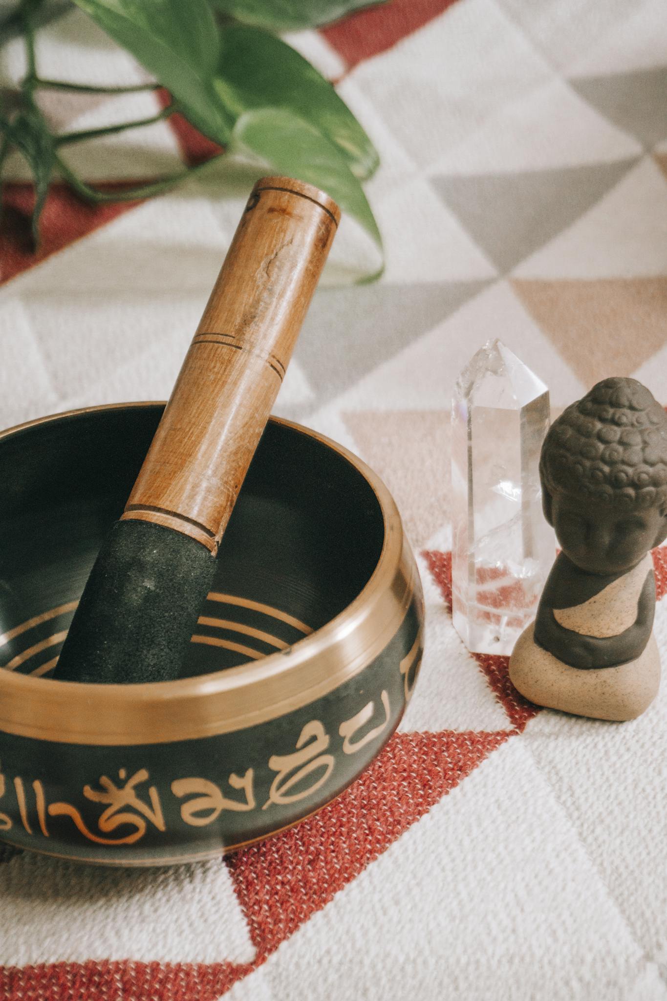 A serene setup featuring a singing bowl, crystal, and Buddha statue on a patterned surface, creating a tranquil atmosphere.